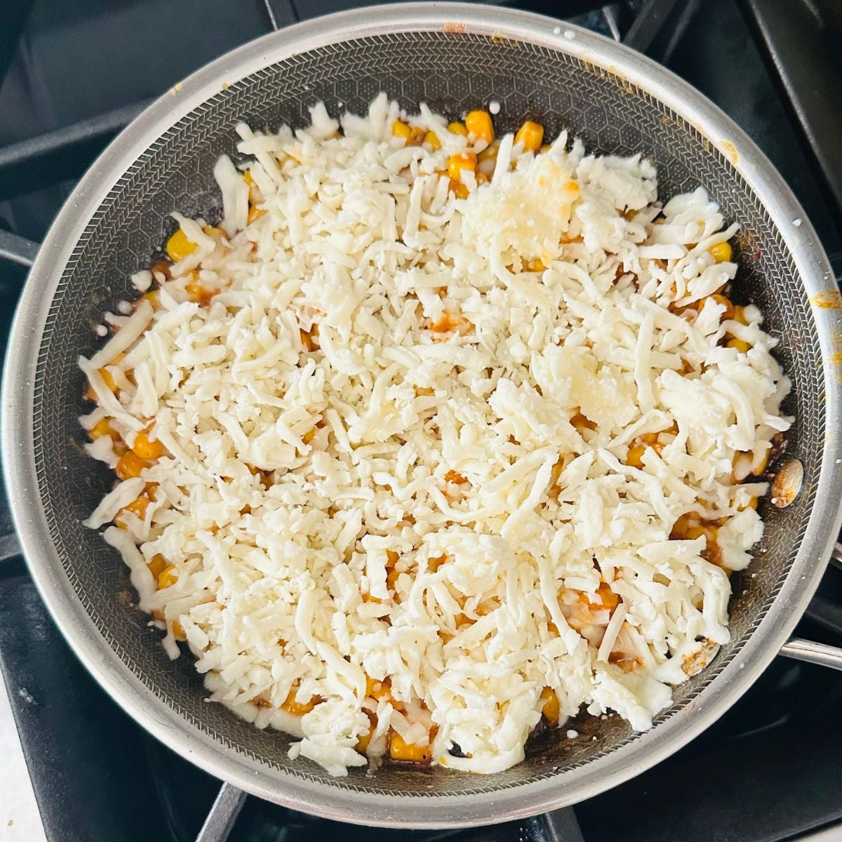 Skillet corn topped with a thick layer of shredded melted cheese before baking.
