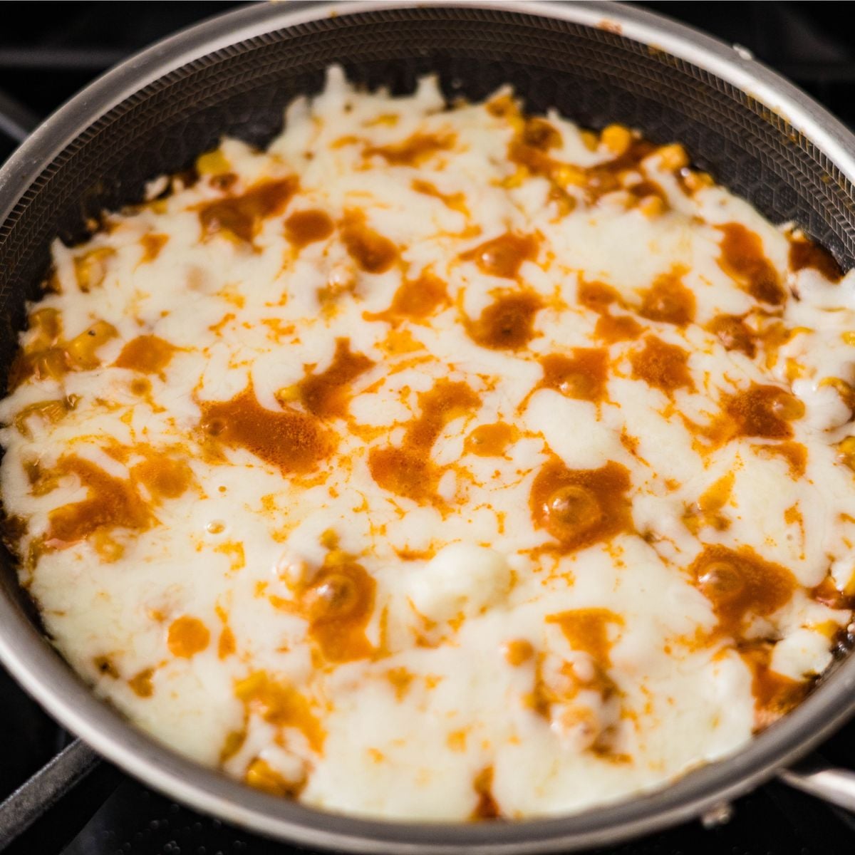 Korean corn cheese in a skillet with melted mozzarella and drizzled Buldak Carbonara sauce.
