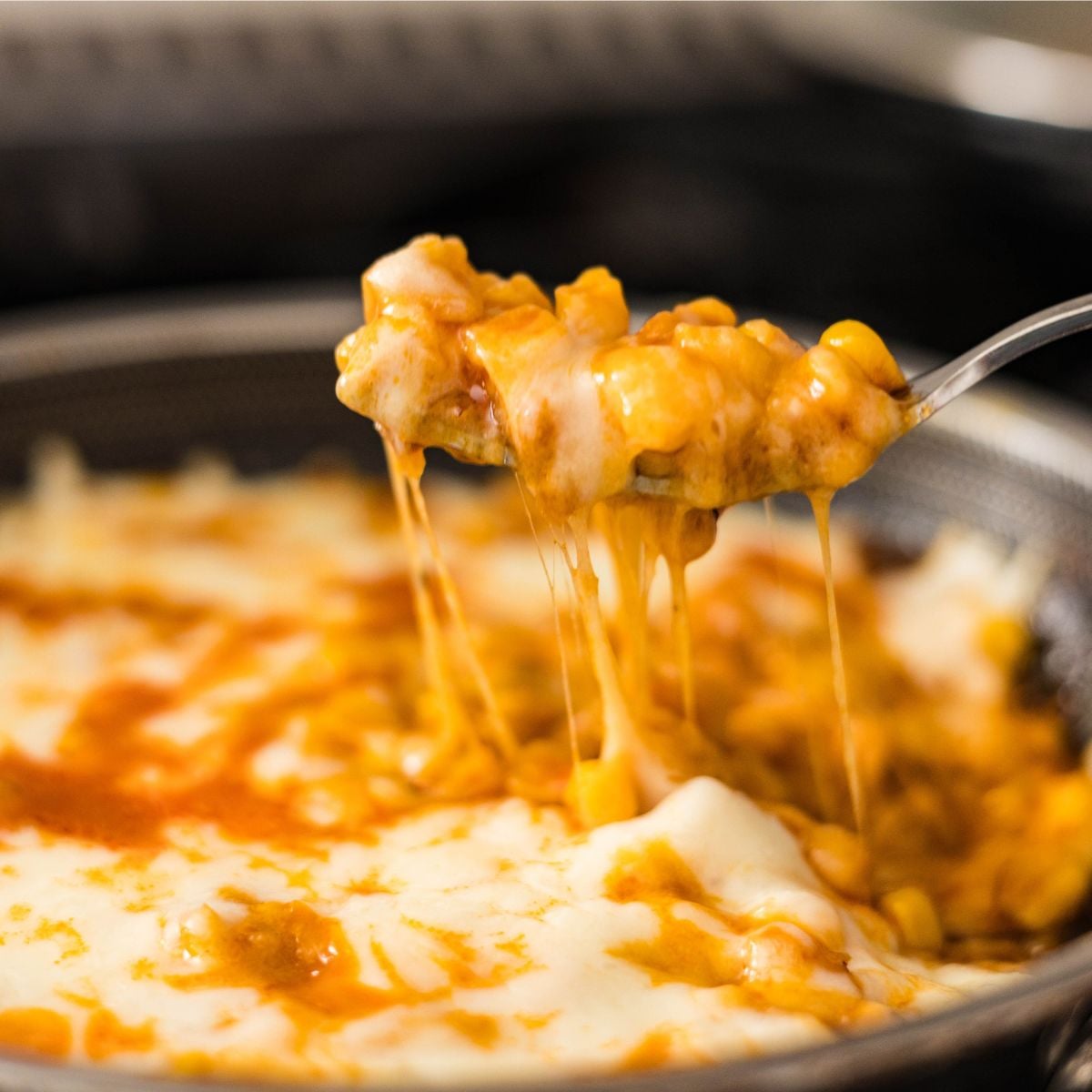 Close-up of spicy cheesy corn on a spoon with melted cheese stretching from the pan.
