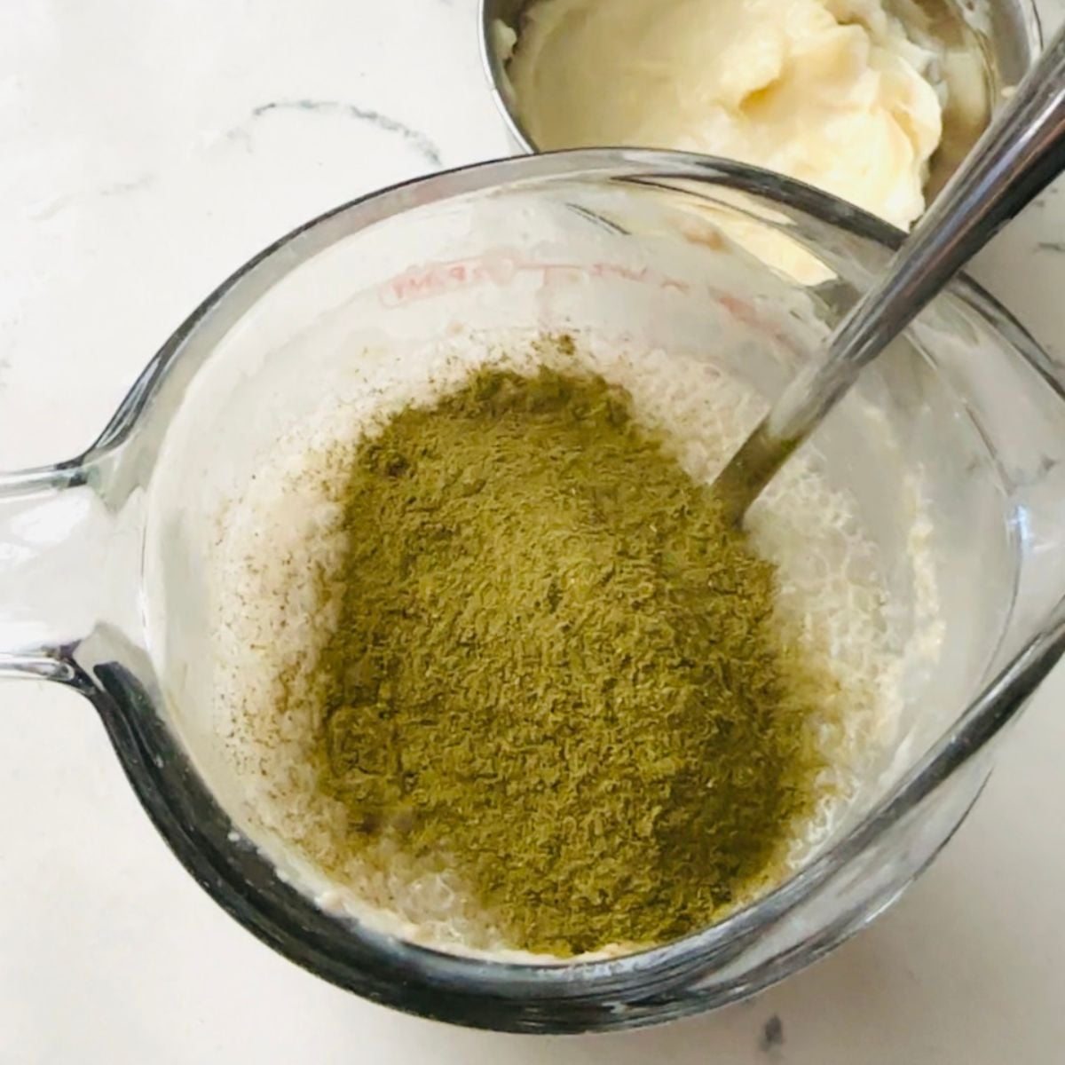 Warm milk and yeast in a measuring cup topped with malunggay powder for malunggay pandesal.