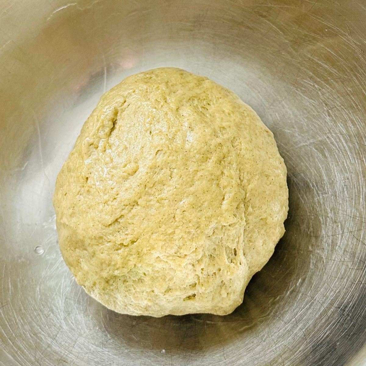 Soft green malunggay pandesal dough in a mixing bowl after kneading and adding butter.