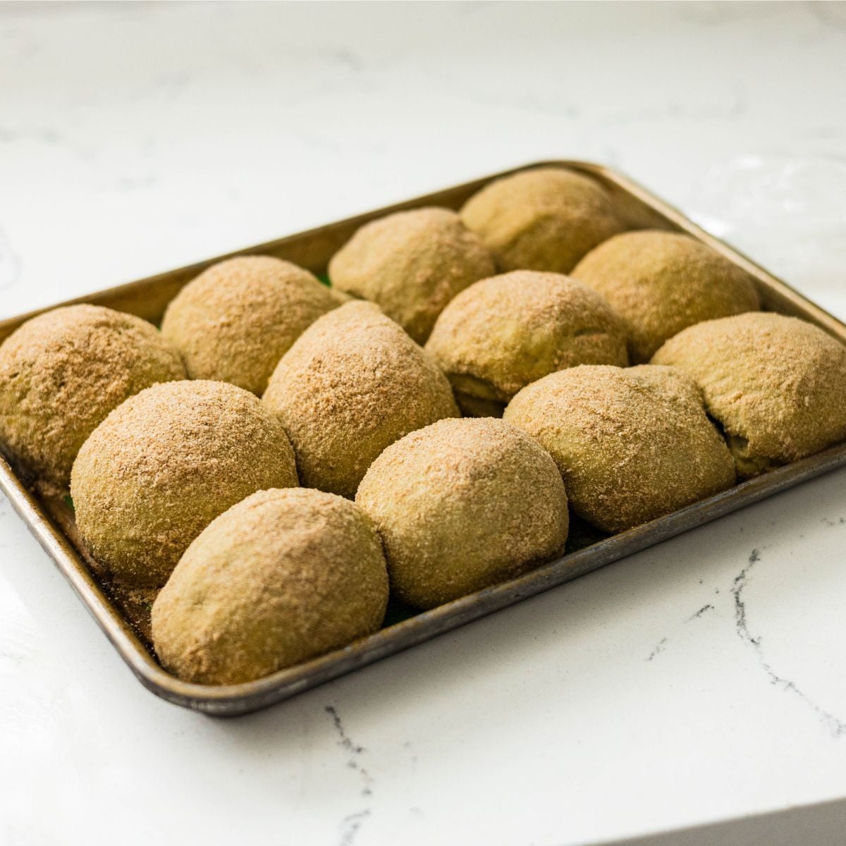 Breadcrumb-coated malunggay pandesal dough balls on a baking sheet before the second rise.