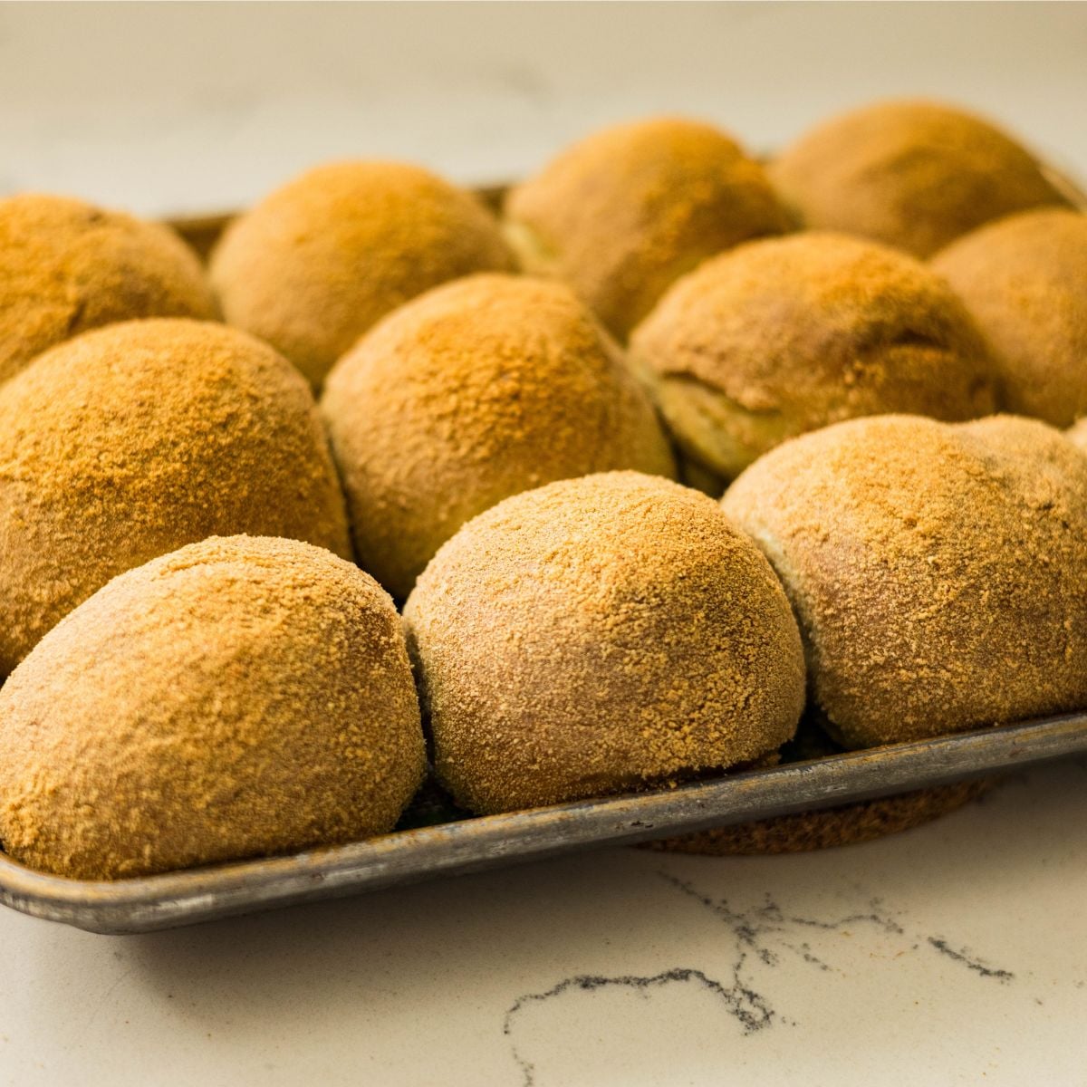 Freshly baked malunggay pandesal rolls coated in breadcrumbs on a sheet pan.