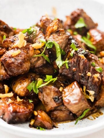 Close-up of glossy beef salpicao pieces topped with sliced green chilies and herbs.