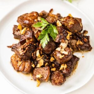 Filipino beef salpicao topped with plenty of crispy garlic and fresh parsley on a white plate.