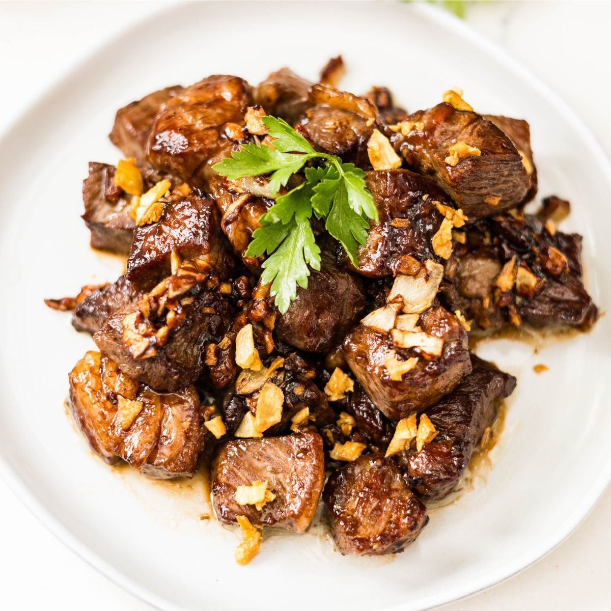 Filipino beef salpicao topped with plenty of crispy garlic and fresh parsley on a white plate.