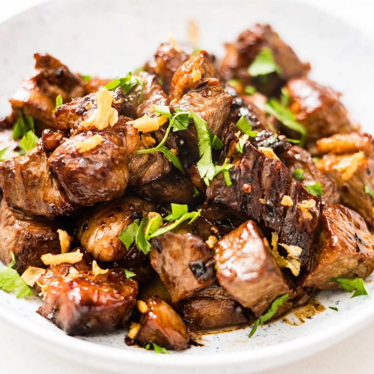 Close-up of glossy beef salpicao pieces topped with sliced green chilies and herbs.