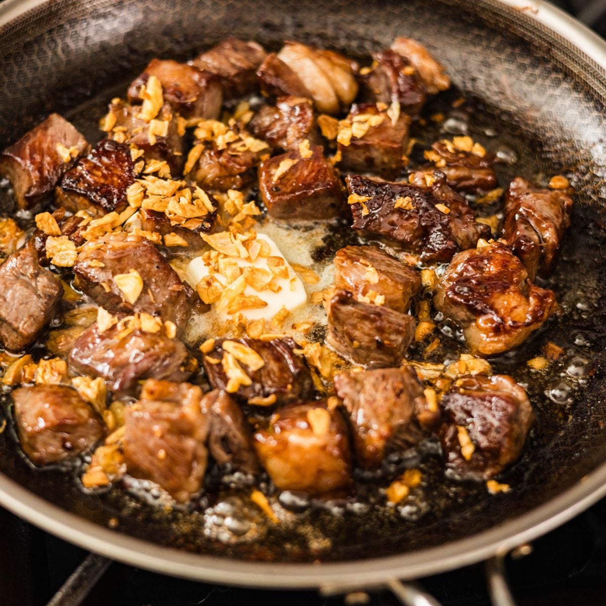 Seared ribeye cubes tossed with butter and crispy garlic in a skillet for beef salpicao.