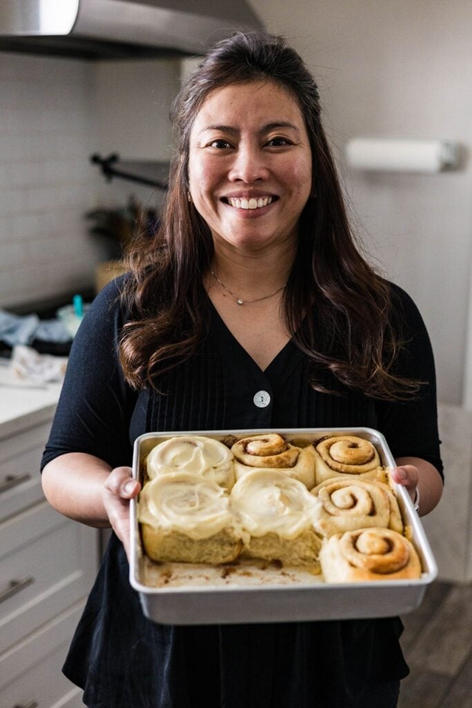 Smiling woman holding a pan of homemade classic cinnamon rolls with cream cheese frosting