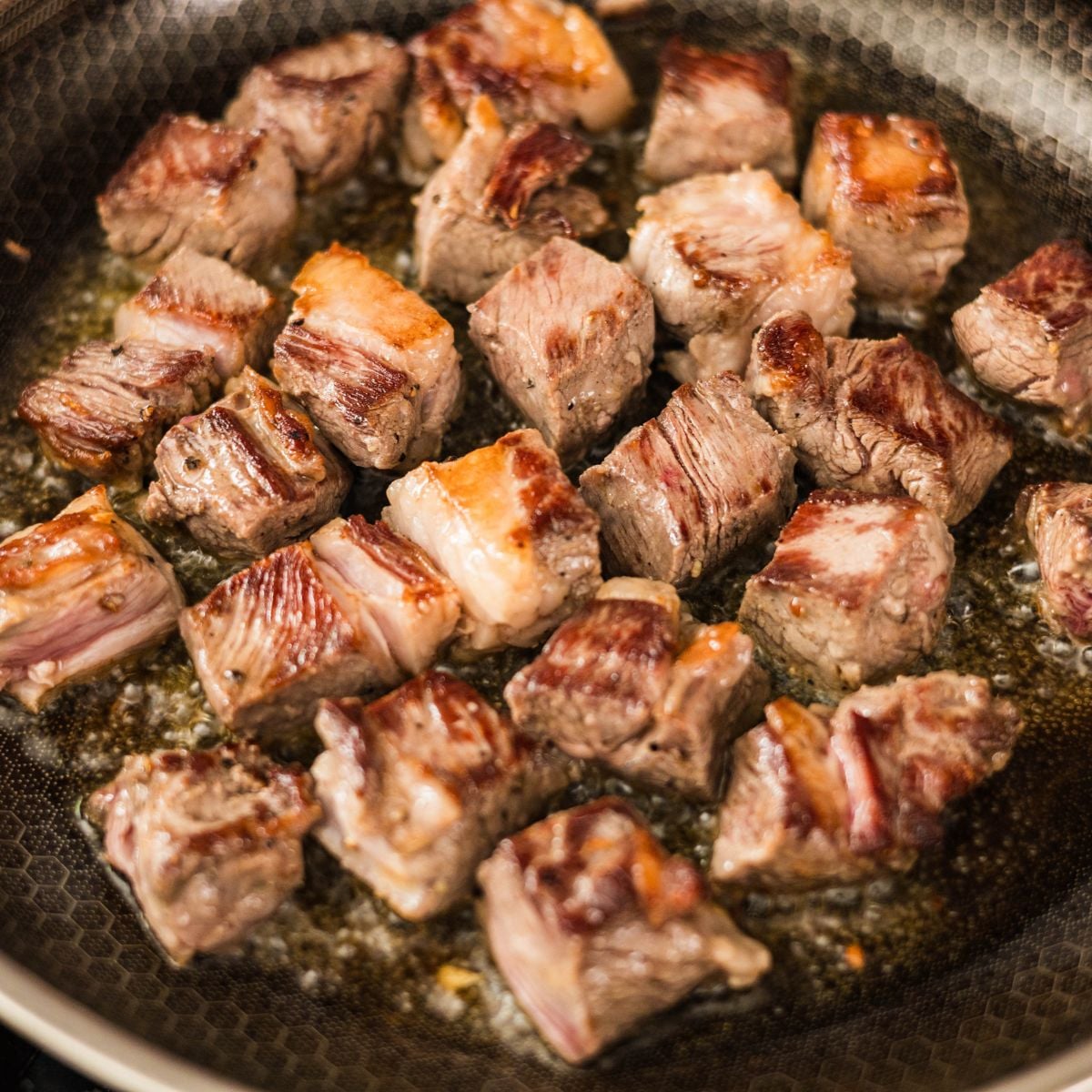 Cubed ribeye steak browned in a skillet with oil for Filipino beef salpicao.