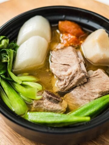 Bowl of pork sinigang with spare ribs, bok choy, okra, radish, taro, and tomato in broth.