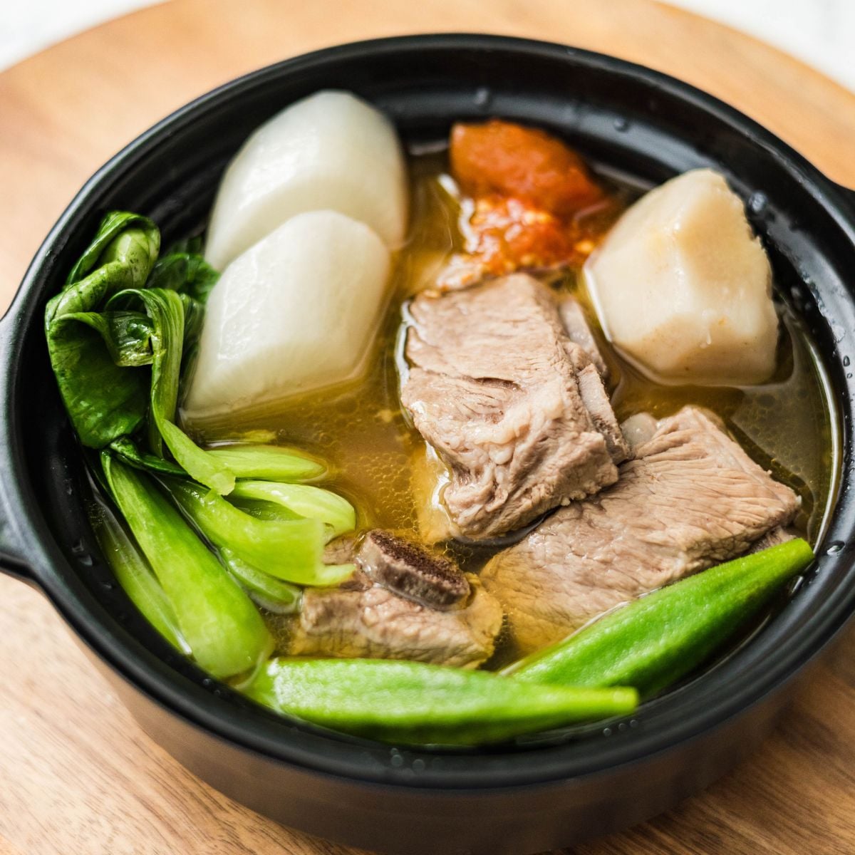 Bowl of pork sinigang with spare ribs, bok choy, okra, radish, taro, and tomato in broth.