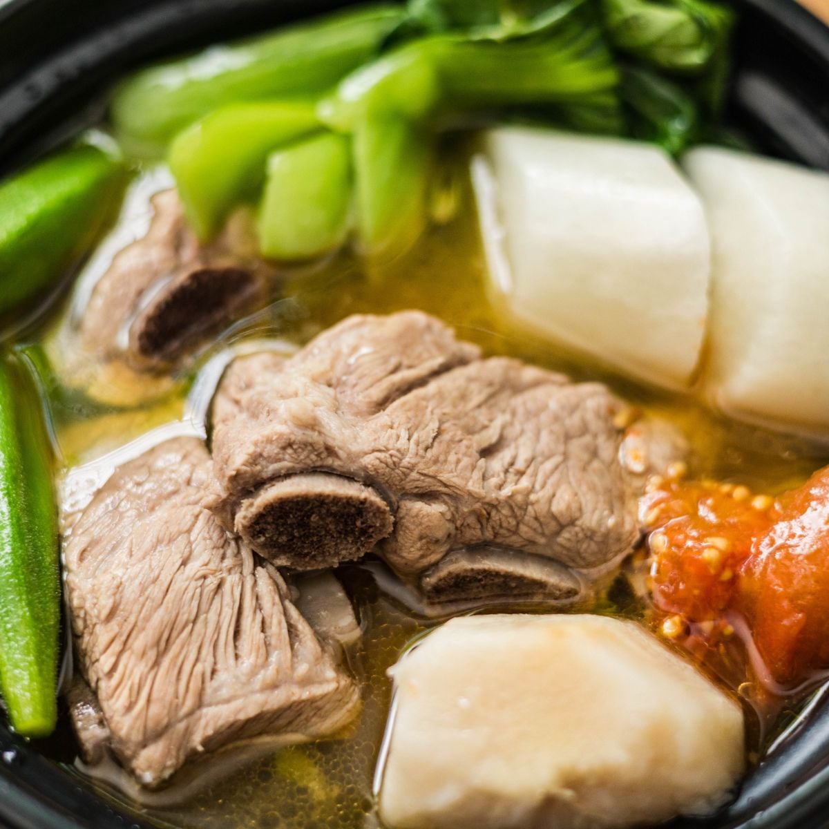 Close-up of pork sinigang with tender spare ribs, radish, okra, bok choy, and tomato in sour broth.