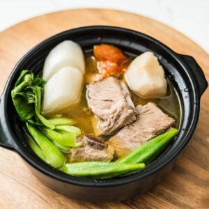 Pork sinigang with spare ribs served in a black bowl with radish, taro, bok choy, okra, and tomato.