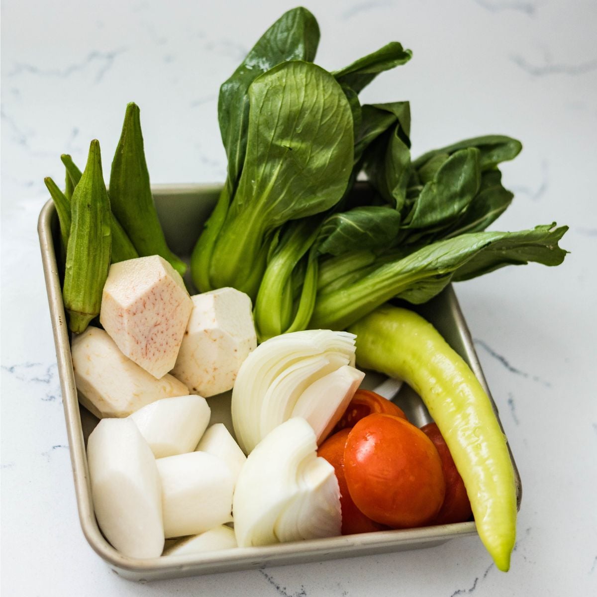 Tray of sinigang ingredients with bok choy, okra, taro, radish, onion, tomato, and green chili.