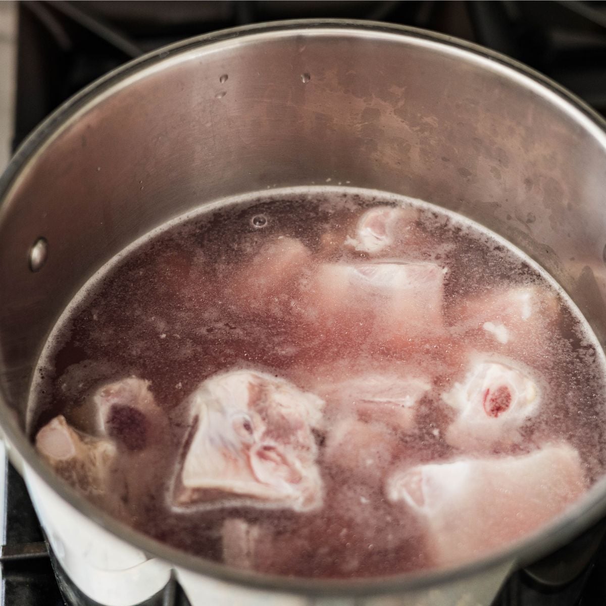Pork spare ribs simmering in a pot during the parboiling step.