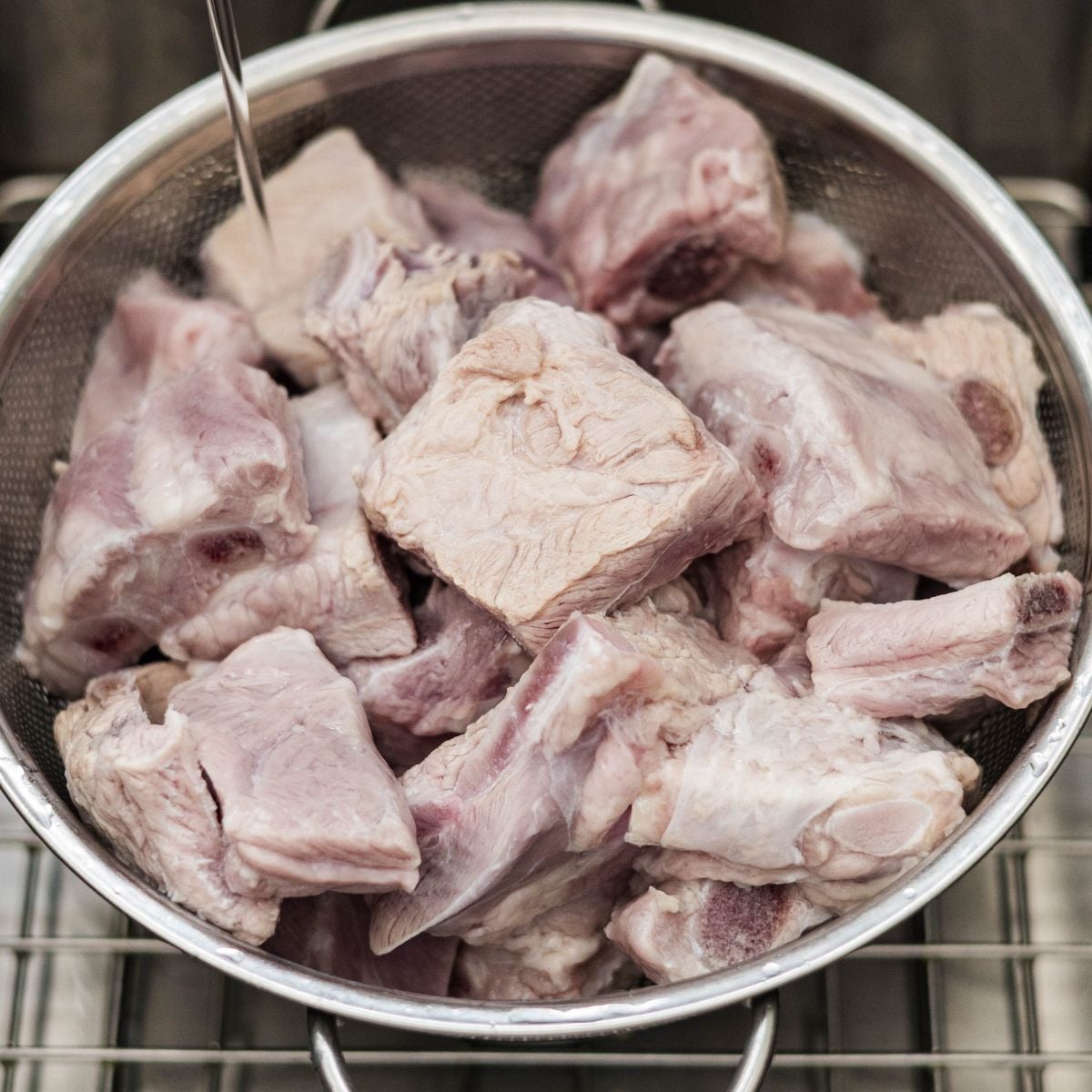 Pork spare ribs draining in a colander under running water in the sink.