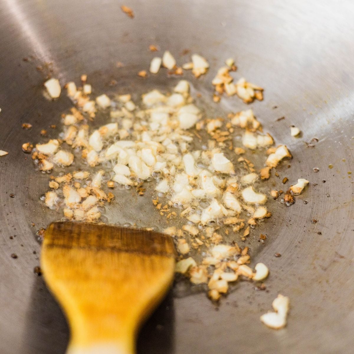 Chopped garlic toasting in hot oil in a wok for homemade garlic fried rice.
