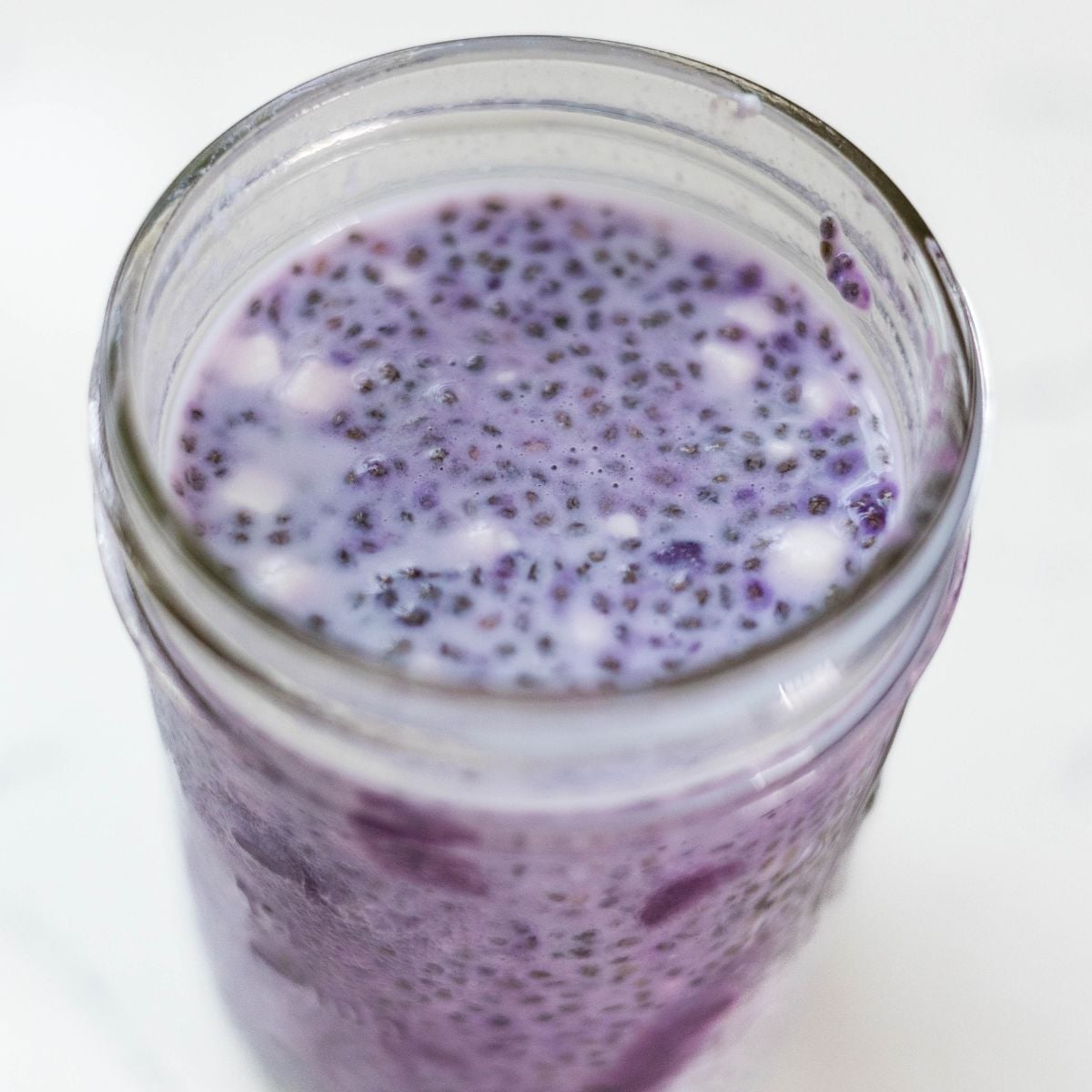 Close-up of creamy ube chia pudding with cottage cheese and chunks of ube halaya in a glass jar