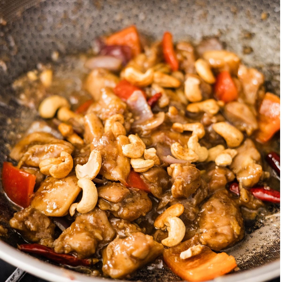 Cashew chicken stir fry with glossy sauce, red bell peppers, onions, and cashews added in the wok.