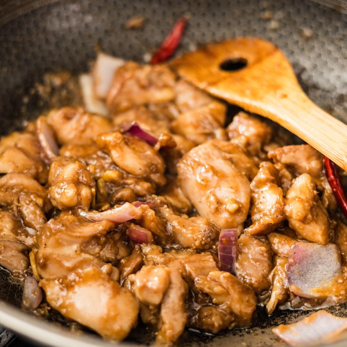 Saucy chicken stir fry cooking in a wok with red onions and dried red chilies.