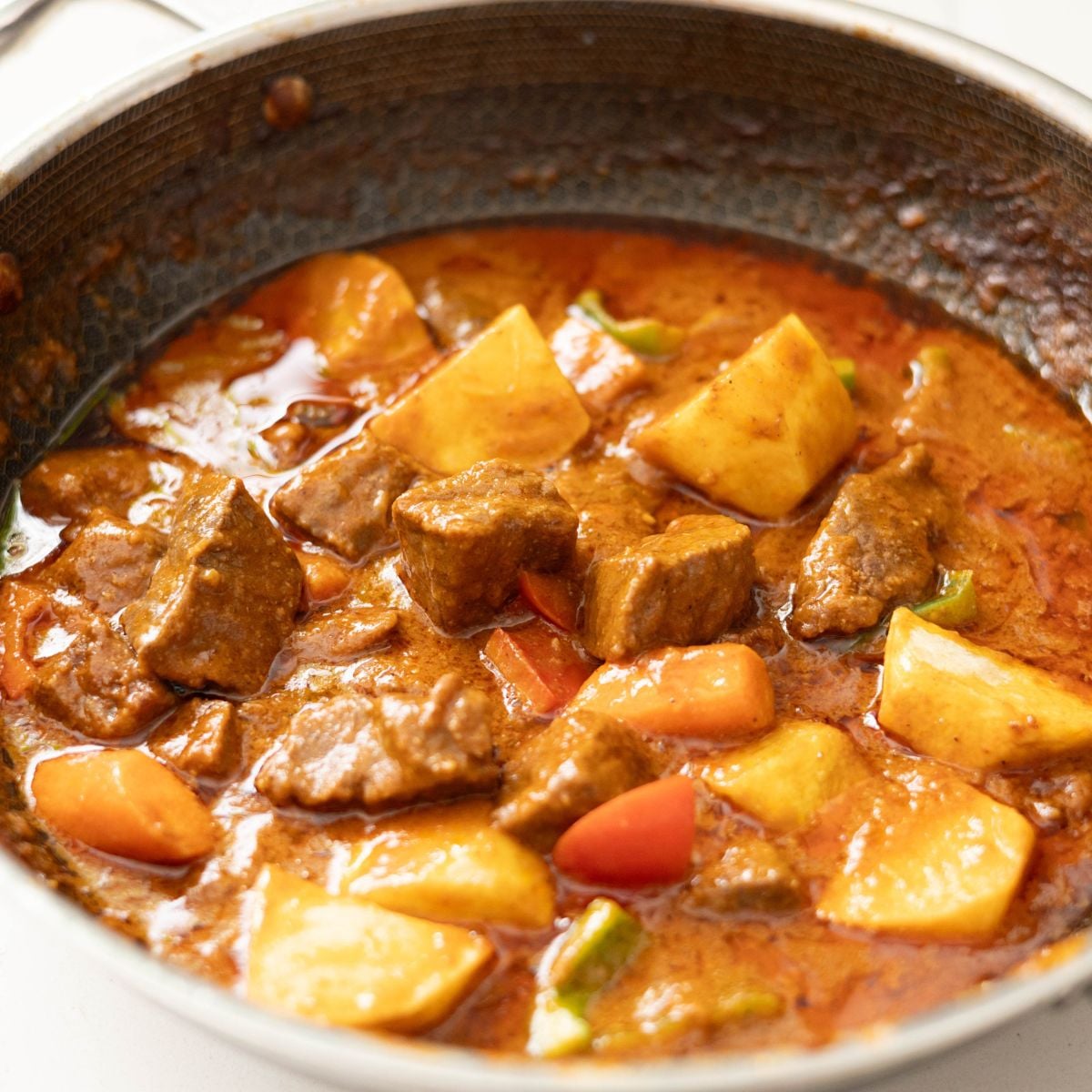 Tender beef chunks cooking in a savory tomato-based caldereta sauce with cheese