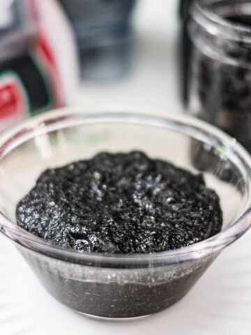 Homemade black sesame paste in a glass bowl with black sesame seeds in the background.