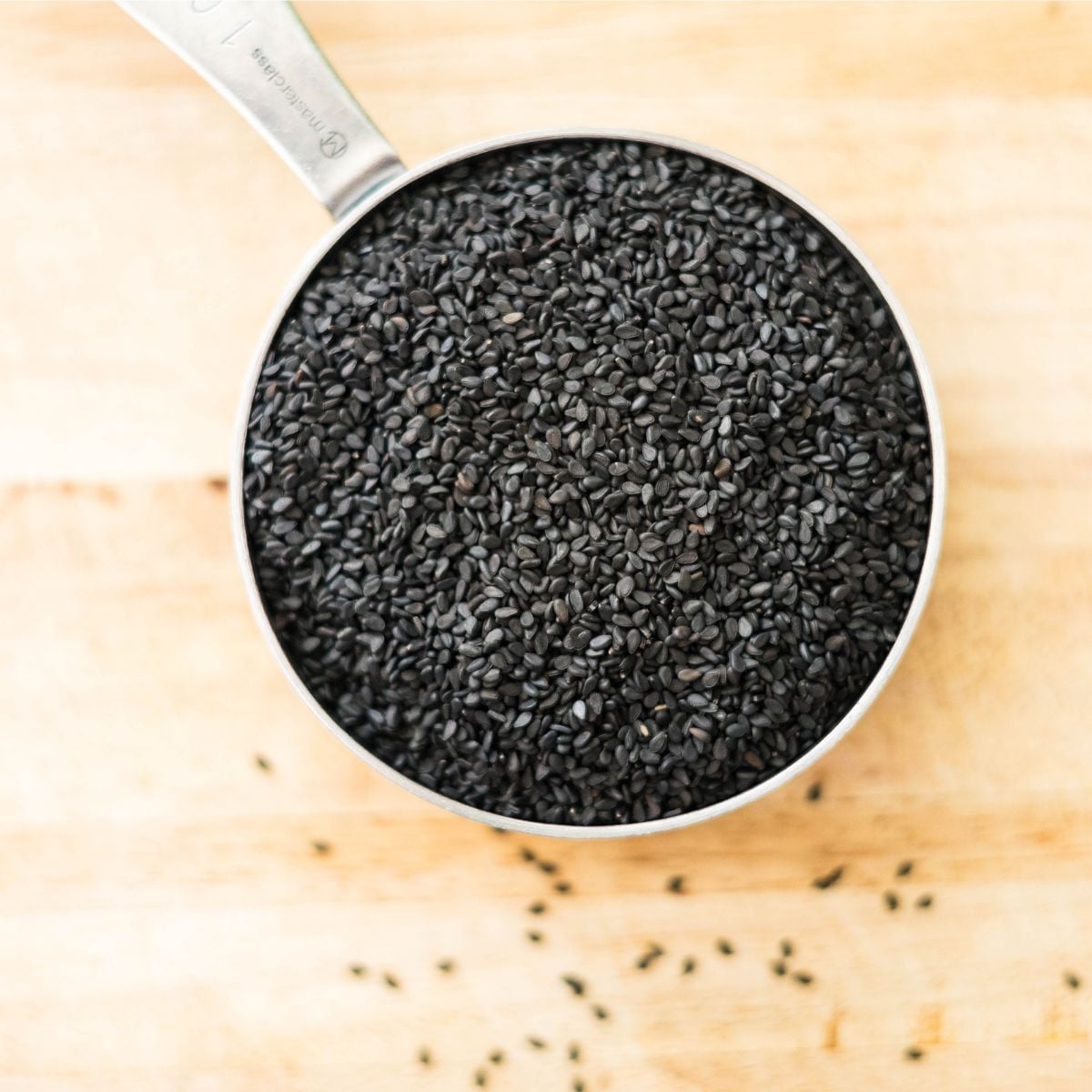 Black sesame seeds measured in a metal cup on a wooden board.