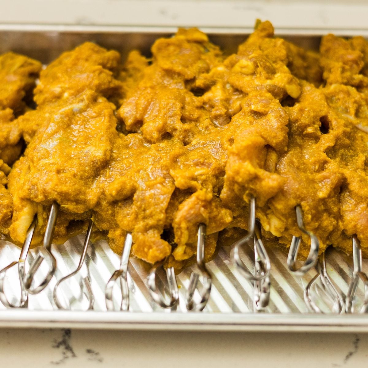 Marinated chicken thighs threaded onto metal skewers and arranged on a tray before grilling.