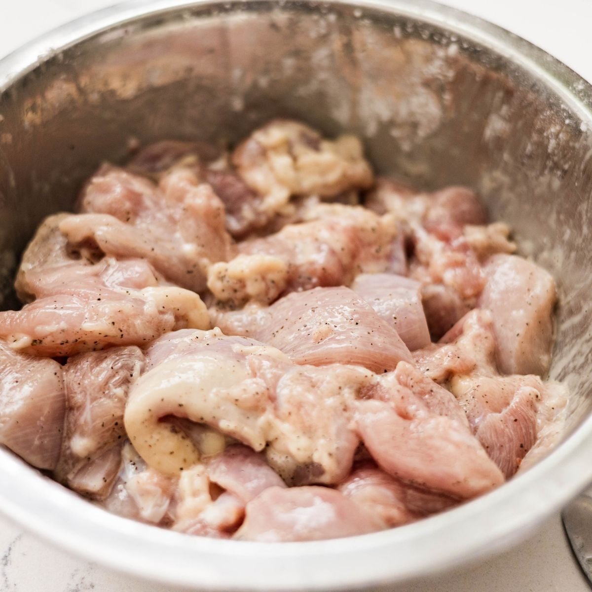 Raw chicken thighs coated with seasoning and cornstarch in a mixing bowl.