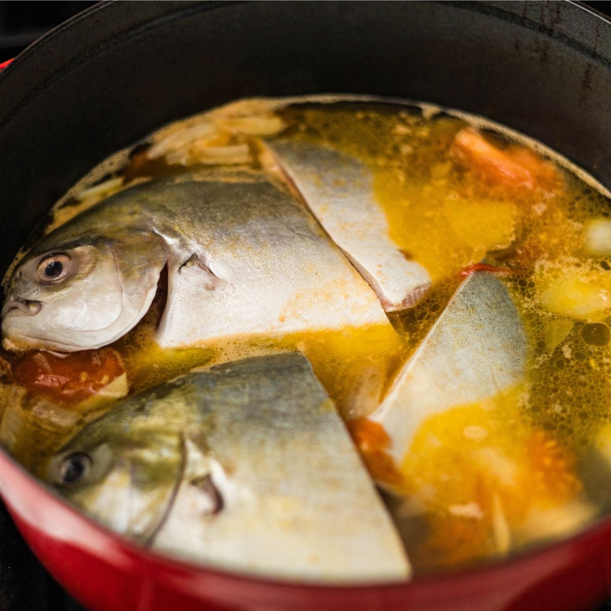 Fresh pompano fish pieces cooking in a tangy sinigang sa miso broth with tomatoes, onions, and ginger.