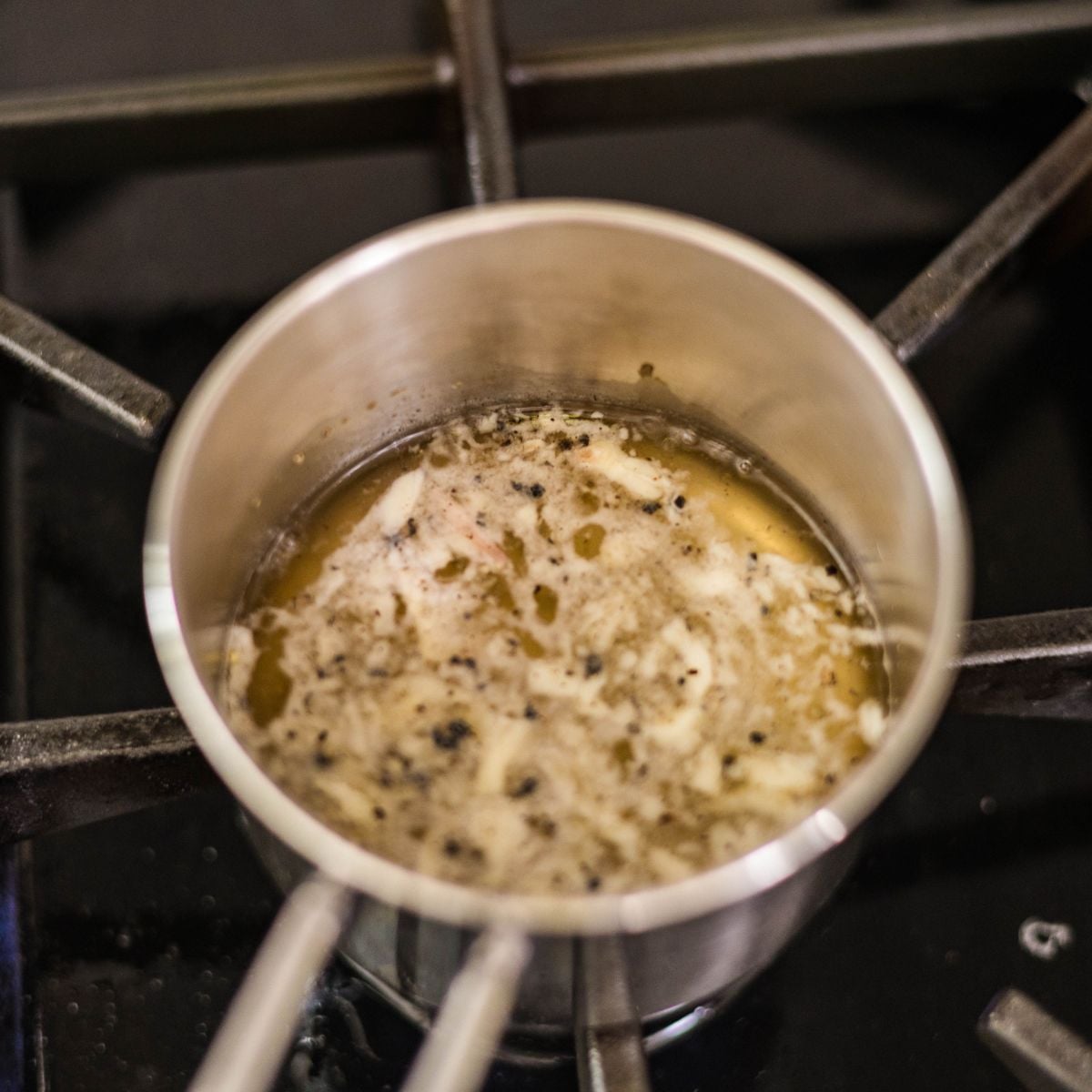 Cooked garlic vinegar dressing for Filipino eggplant salad simmering in a small saucepan.