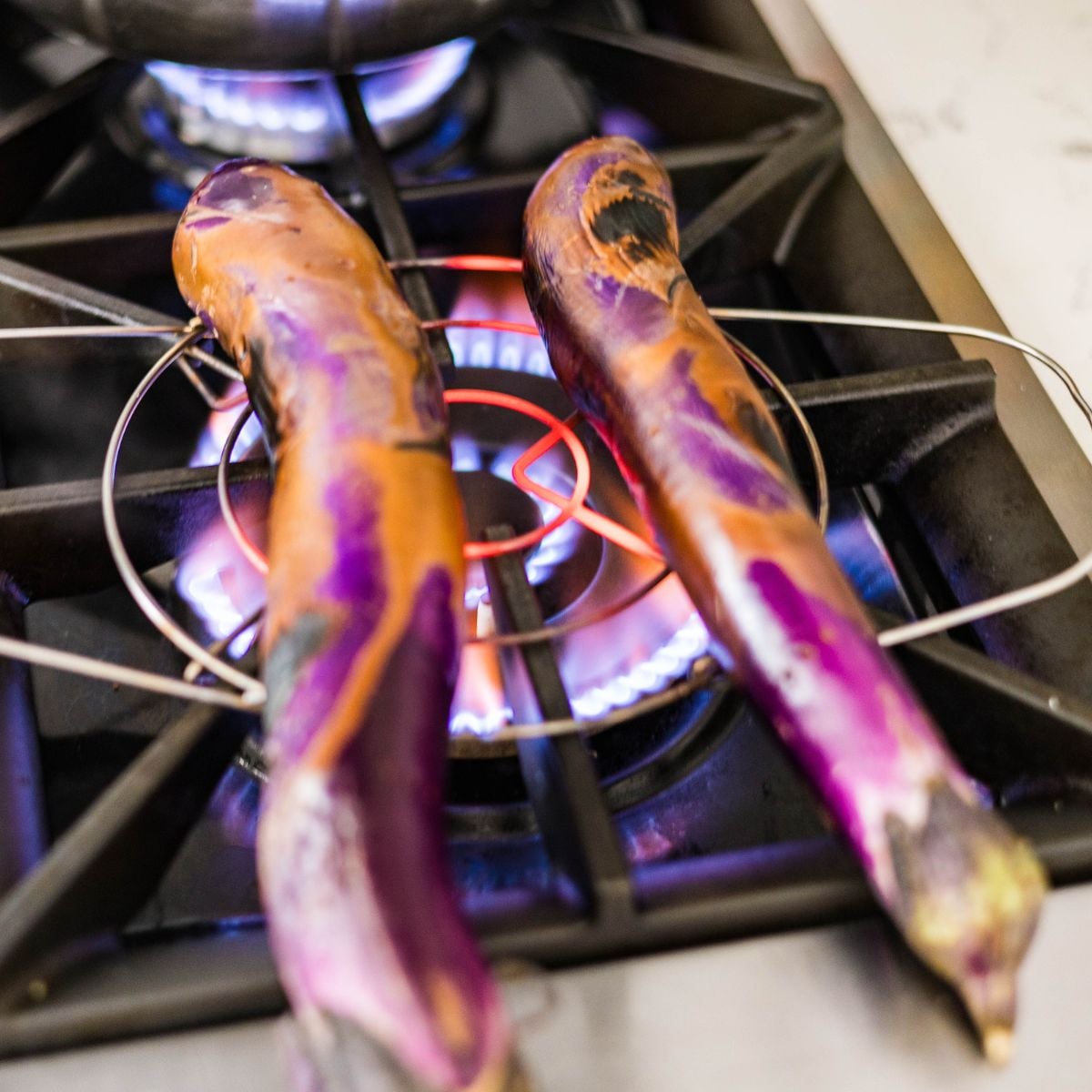 Filipino eggplants charring over a gas stove flame for ensaladang talong.