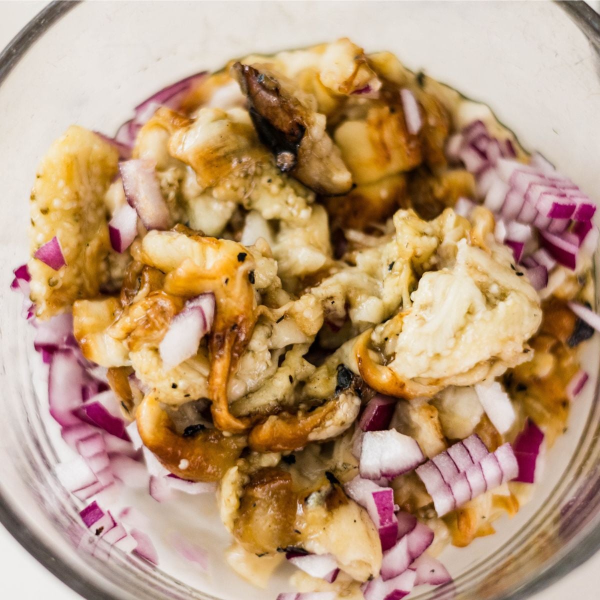 Chopped grilled eggplant and red onion in a bowl for ensaladang talong.