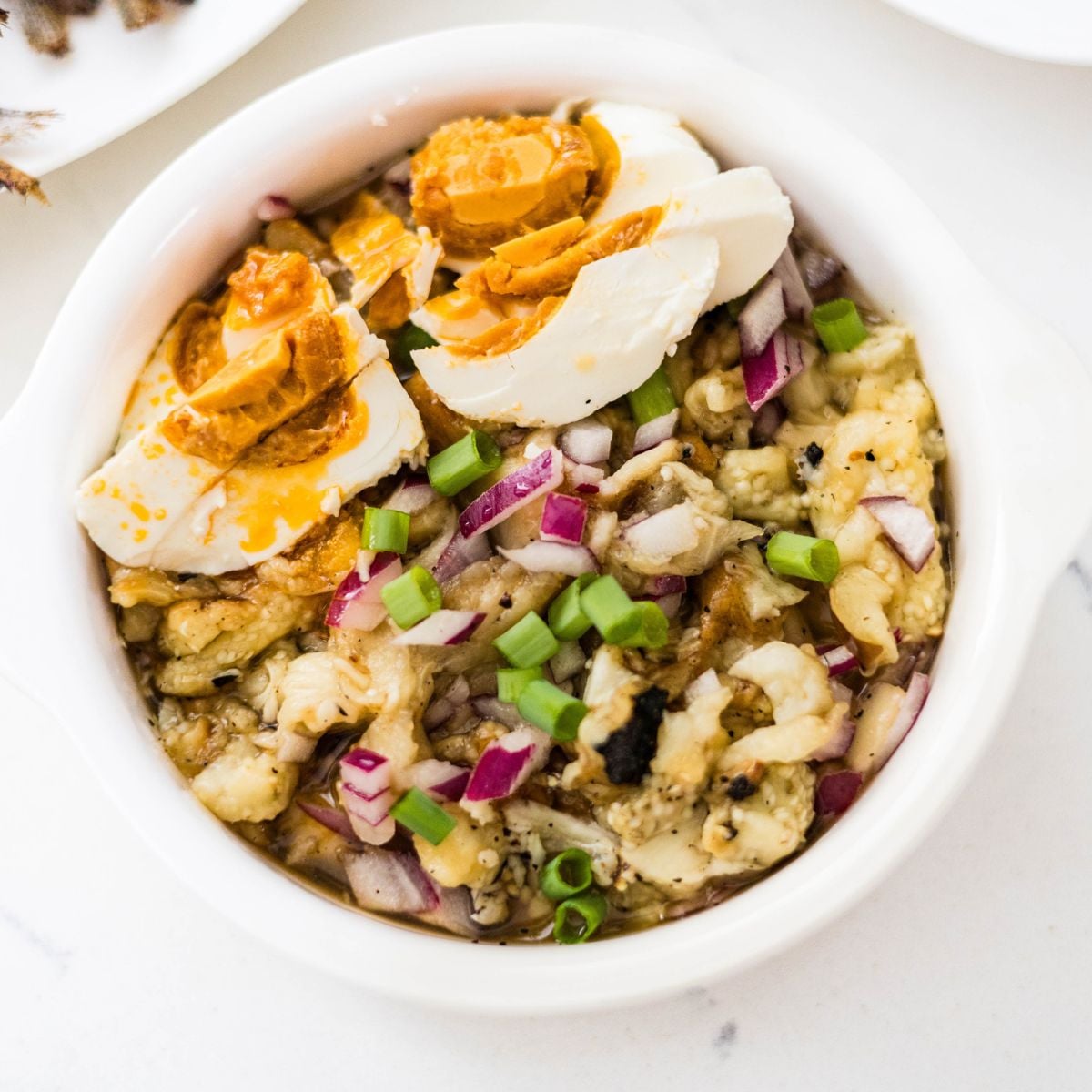 Filipino eggplant salad with salted egg, red onion, and green onions in a serving bowl.