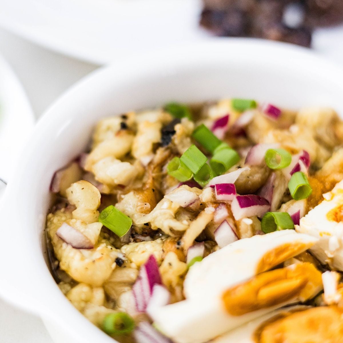 Filipino eggplant salad with salted egg, red onion, and green onions in a serving bowl.