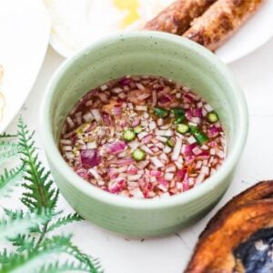 Filipino vinegar dipping sauce with red onion, garlic, calamansi, and Thai chili in a green bowl