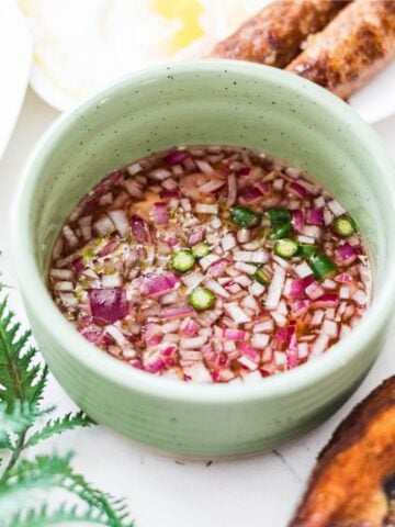 Filipino vinegar dipping sauce with red onion, garlic, calamansi, and Thai chili in a green bowl