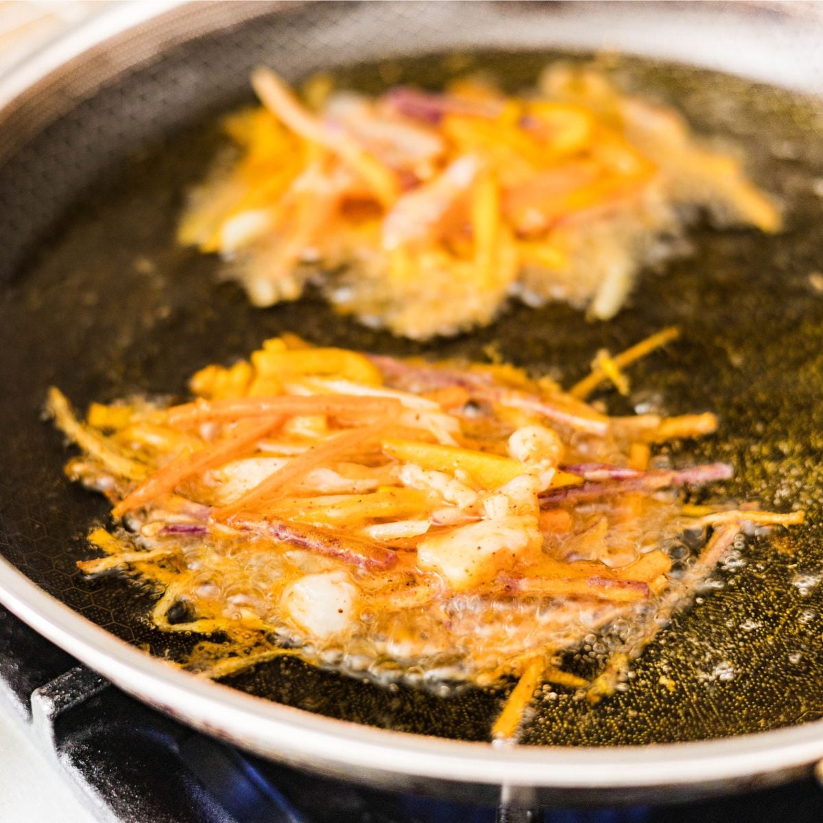 Crispy okoy vegetable fritters with shrimp frying in hot oil in a skillet.