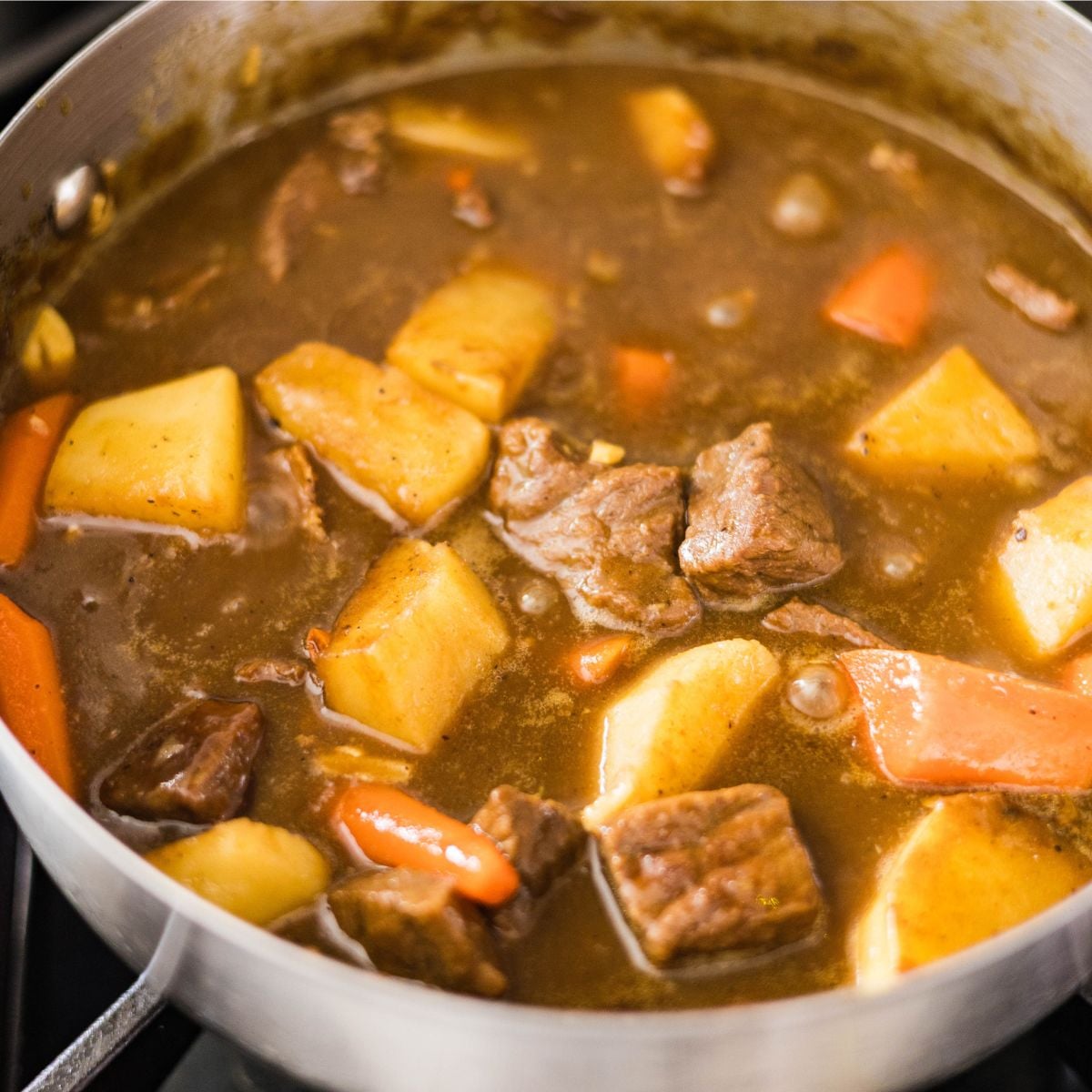 Japanese beef curry simmering with beef chunks, potatoes, and carrots in a pot.