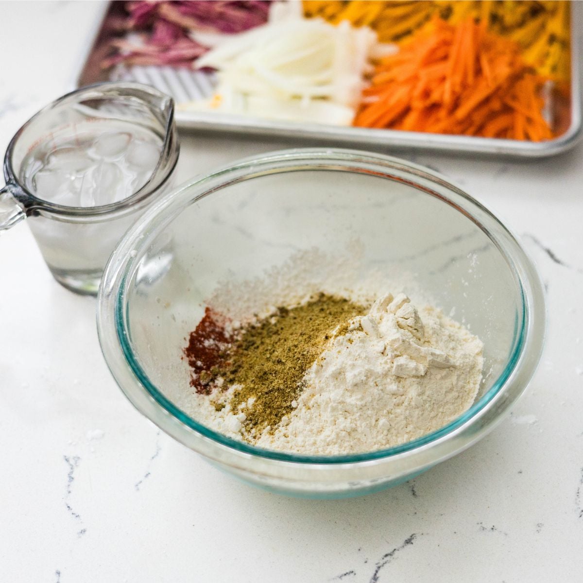 Bowl of seasoned flour mixture with ice water and julienned vegetables prepared for crispy okoy batter.