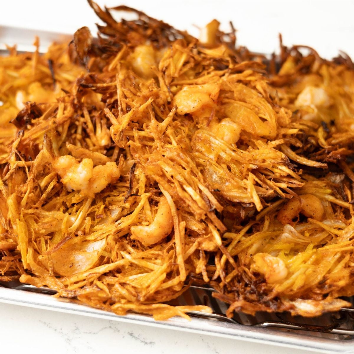 Golden brown crispy okoy fritters with shrimp and shredded vegetables on a cooling rack.