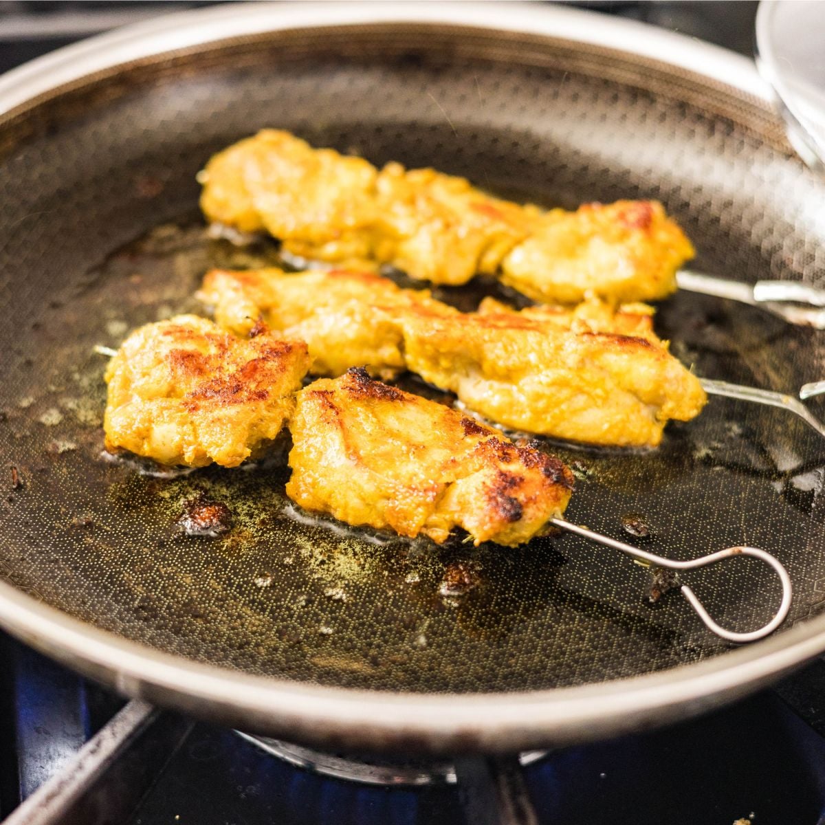 Chicken satay skewers cooking in a hot pan until golden brown and lightly charred.