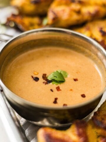 Creamy peanut dipping sauce topped with chili flakes and cilantro, served beside chicken satay skewers.