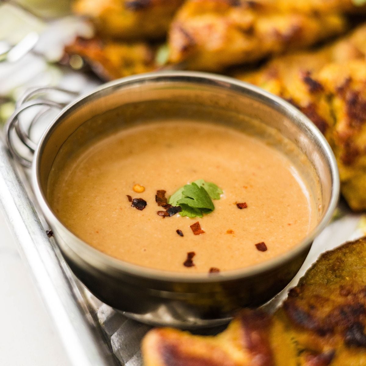 Creamy peanut dipping sauce topped with chili flakes and cilantro, served beside chicken satay skewers.