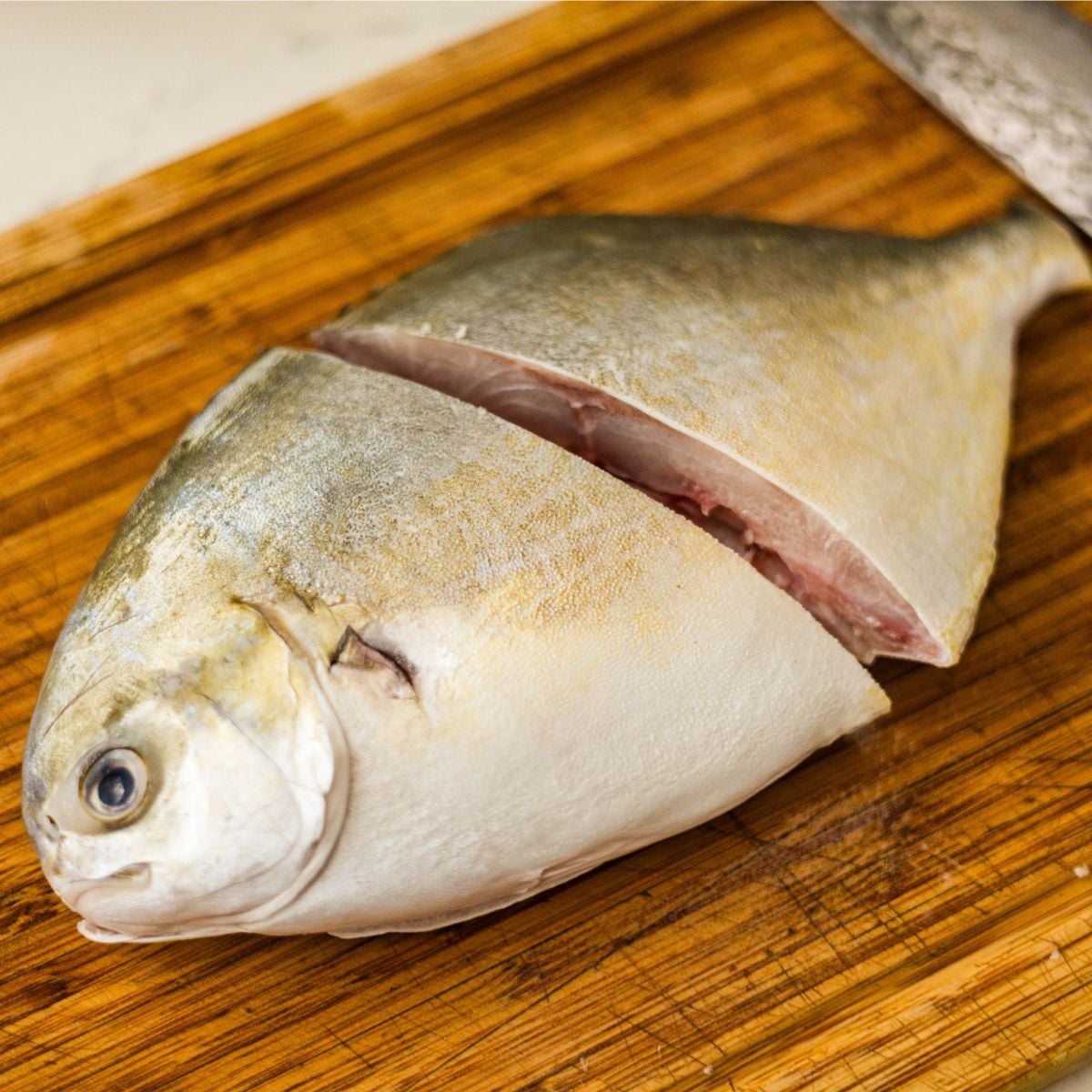 Fresh pompano fish cleaned and sliced on a wooden cutting board for Filipino sinigang sa miso.