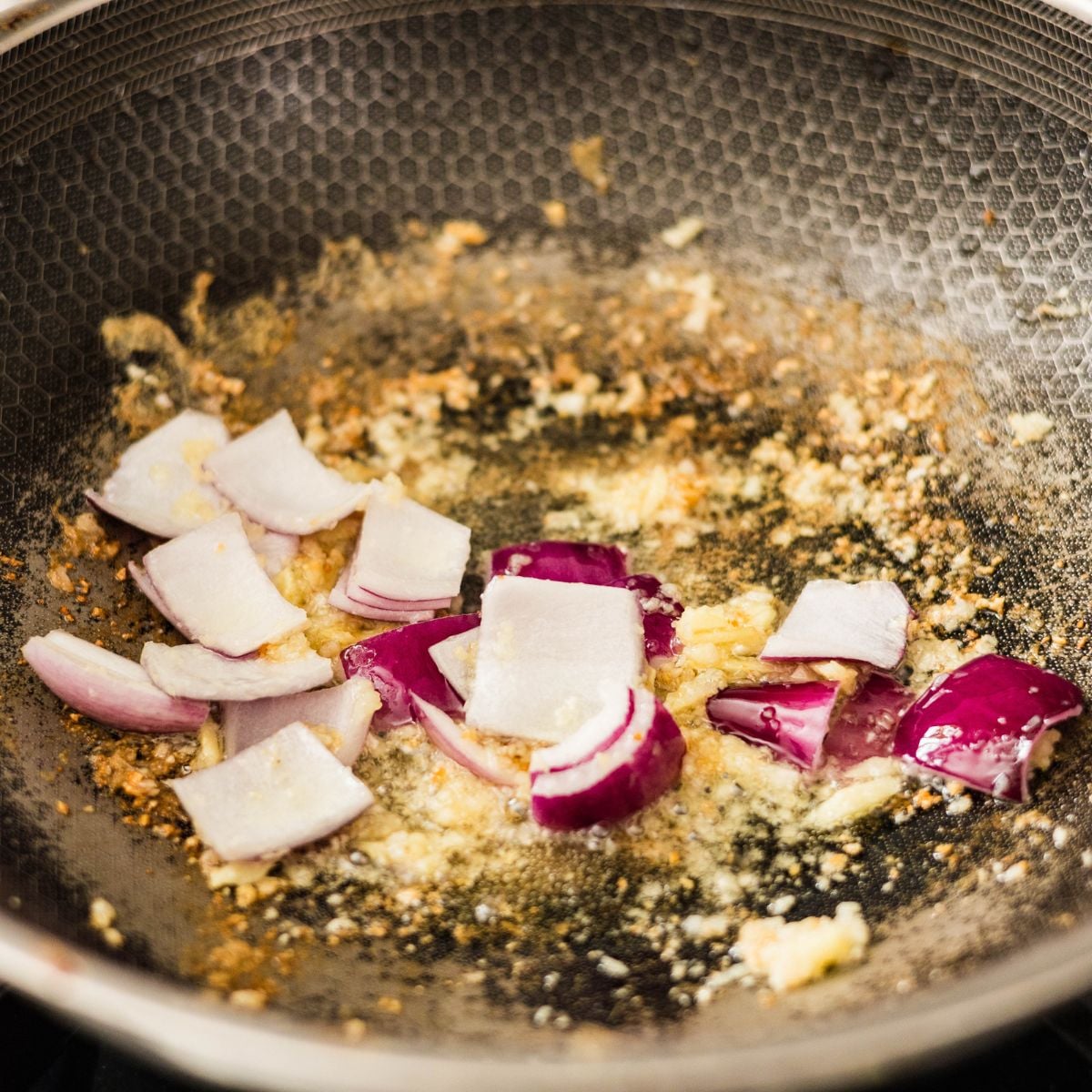 Garlic and red onion sautรฉing in a wok for cashew chicken stir fry.