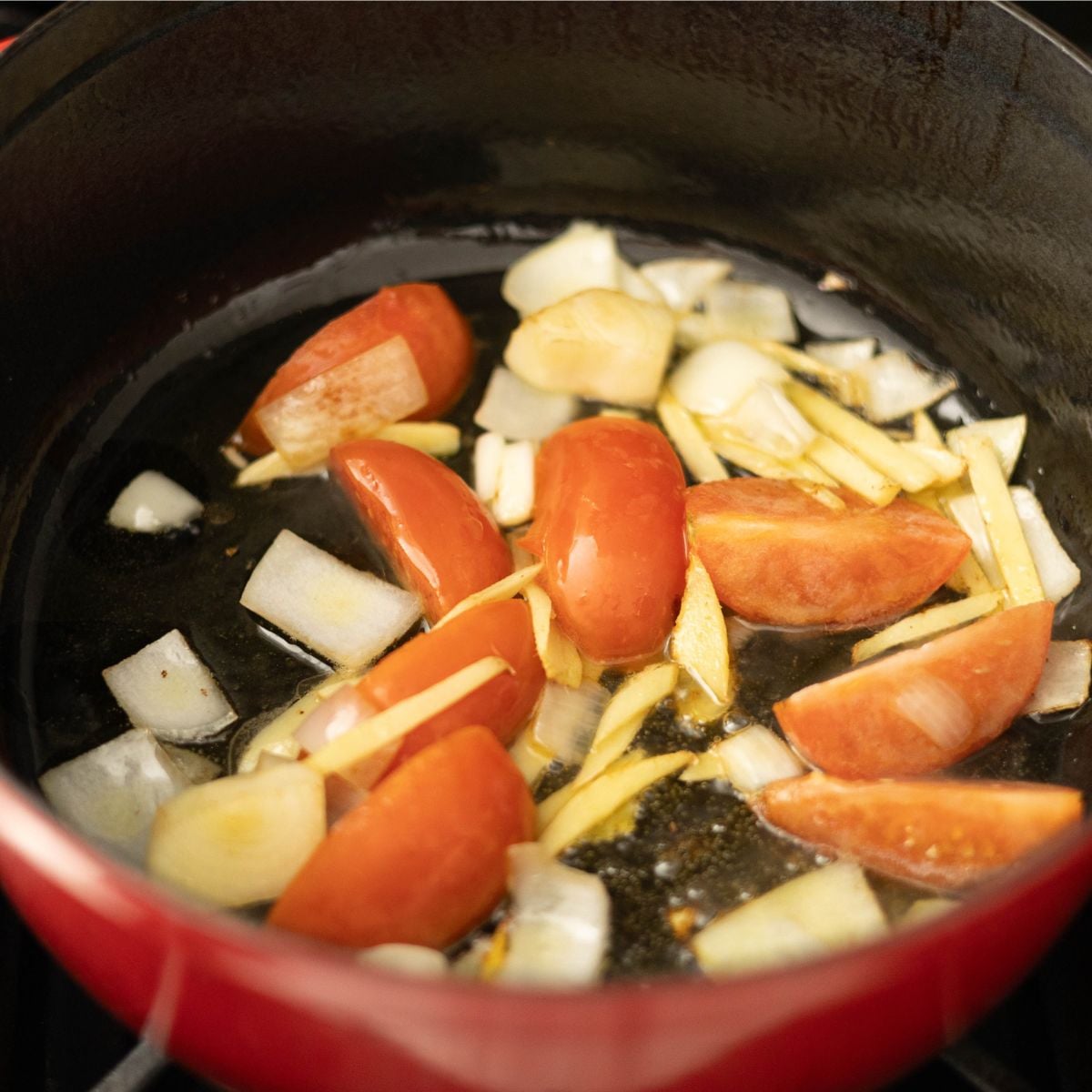 Onions, ginger, garlic, and tomatoes sautéing in a red pot as the flavor base for sinigang sa miso.
