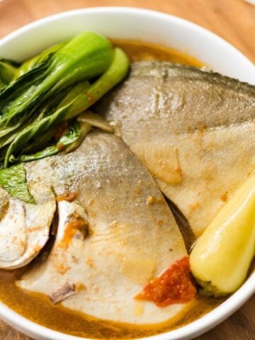 A bowl of sinigang sa miso with pompano, bok choy, tomatoes, and warm sour broth.