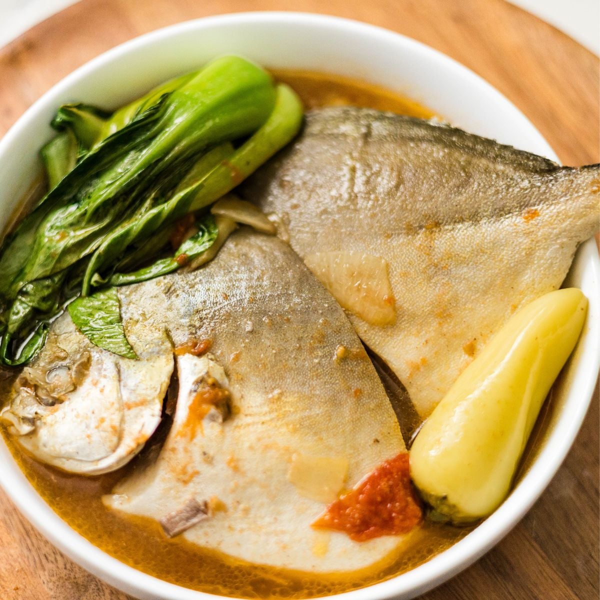 A bowl of sinigang sa miso with pompano, bok choy, tomatoes, and warm sour broth.